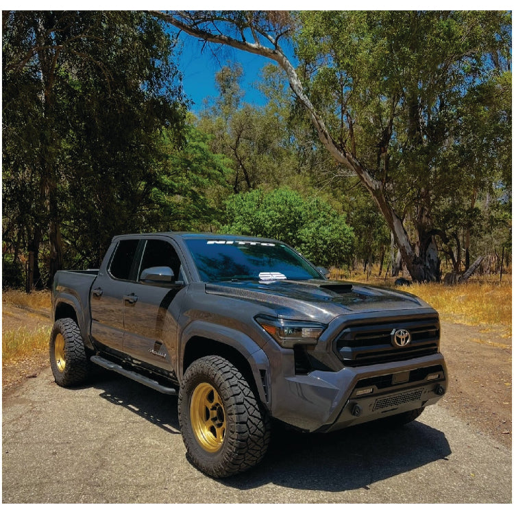 Gray Toyota Tacoma truck with gold  TE37 wheels on a dirt road surrounded by trees